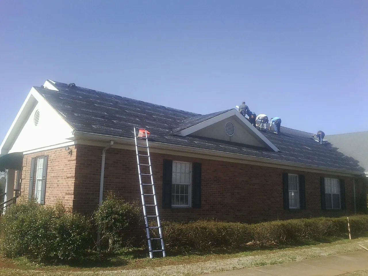 Crew tearing shingles off a brick ranch roof with a ladder set — Metal Roof Repair work by our crew in Waltham