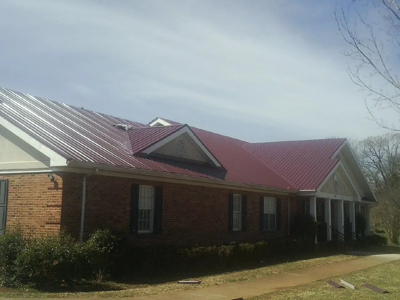 Red metal roof with gabled entries on a long brick building, from a Hail Damage Roof Repair job in Waltham