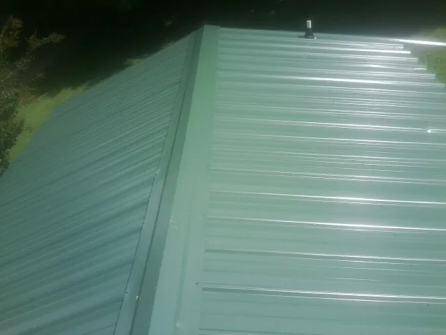 New green metal panels meeting at the ridge of a roof — Flat Roof Repair work by our crew in Waltham