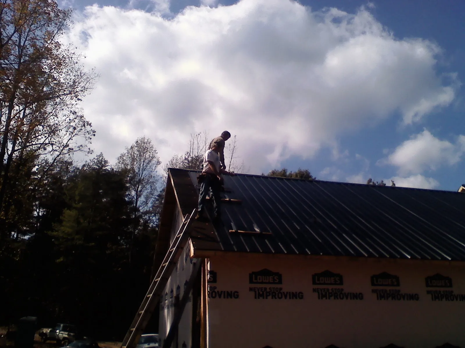 Roofer fastening dark metal panels high against a cloudy sky, from a Roof Inspection job in Waltham