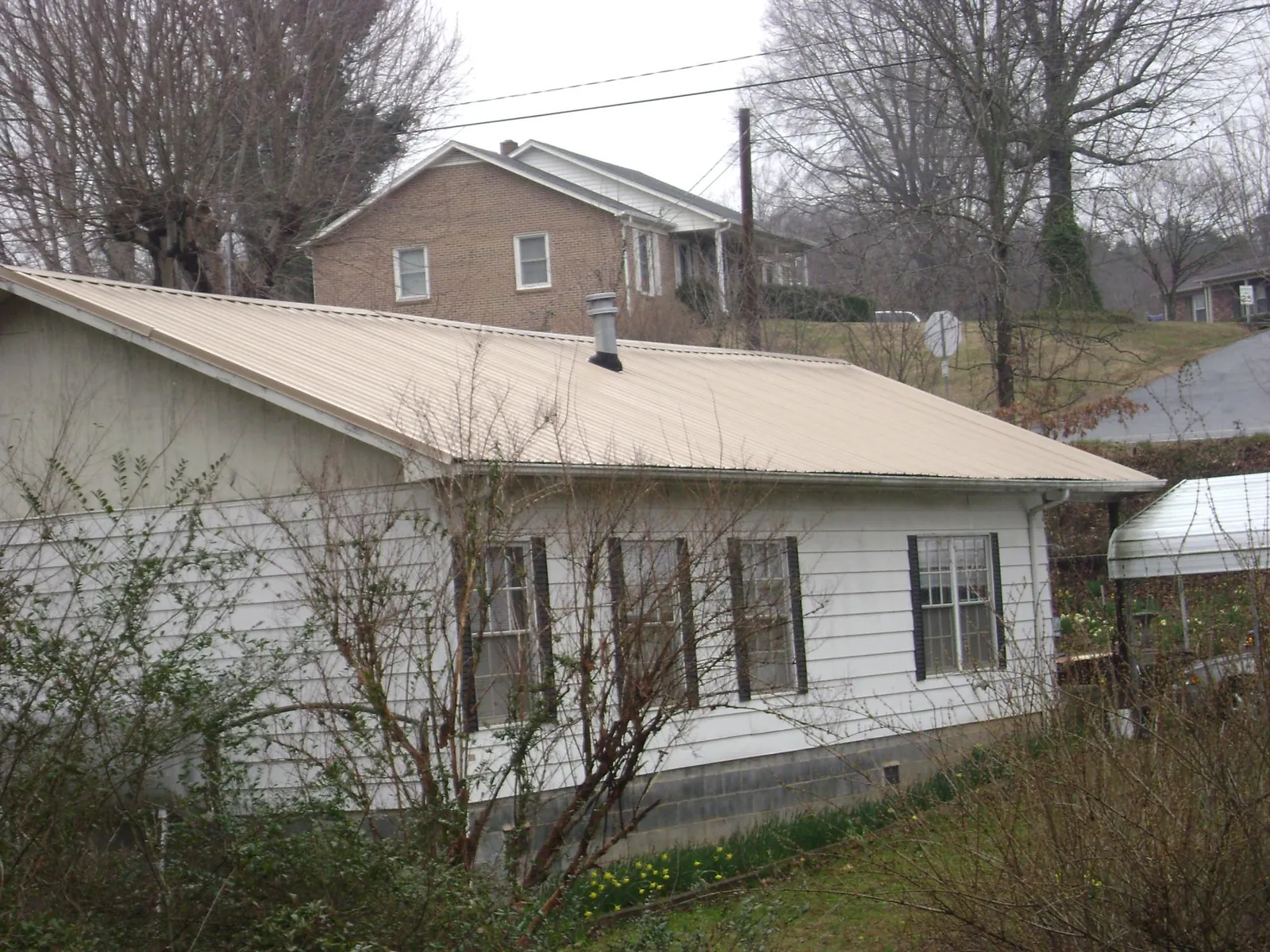 Tan metal roof on a white sided house set into a hillside — Commercial Roofing by Roofing Brothers in Waltham